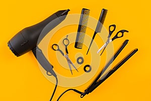 Black hair dryer, comb and scissors on yellow paper background. Top view