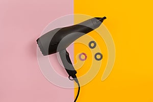 Black hair dryer on pink and yellow paper background. Top view