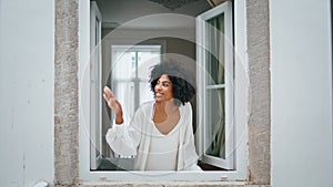Black hair girl waving window morning house. Curly smiling woman peeping outside