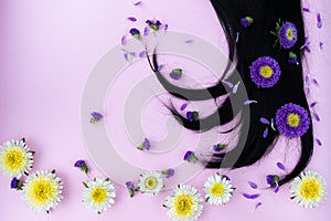 Black hair with yellow and lilac flowers and petals on it. Hair care concept.