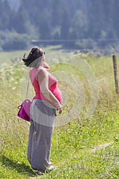 Black-haired pregnant woman against of green forest
