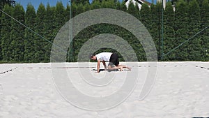 Black-haired, sinewy athlete warms up before a match on a beach volleyball court. An athlete demonstrates the bear walk
