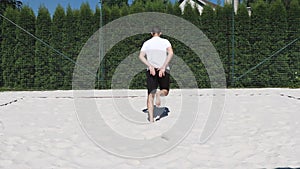 Black-haired, sinewy athlete warms up before a match on a beach volleyball court. Athlete shows stumbling, backward kick