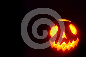 Black Halloween background with a glowing jack-o-lantern. Photo of scary pumpkin