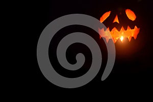 Black Halloween background with a glowing jack-o-lantern. Photo of scary pumpkin