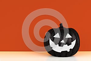 Black Halloween Jack o Lantern decoration on a shelf against an autumn orange background