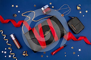 Black hand bag with red ribbon, golden jewelry, woman cosmetics over the dark blue backgroun