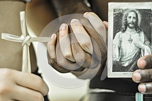 Black hand next to white hand, white woman with a cross in hand, black man with a picture of God in hand