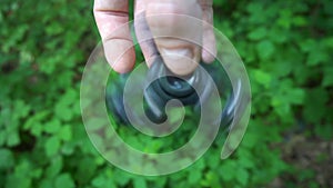Black hand spinner, or fidgeting spinner, rotating on child`s hand.grass background