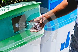 Black hand throwing an empty plastic water bottle in the recycling garbage trash