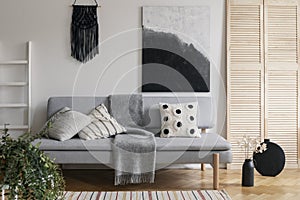 Black handmade macrame and fancy painting on white wall of sophisticated living room interior with grey fashionable couch with