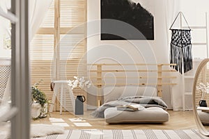 Black handmade macrame on white wooden ladder in bright bedroom interior with wooden furniture and beige futon with grey warm
