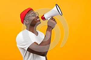 Black handsome smiling american man in white t-shirt speaks news through a megaphone on isolated orange background with