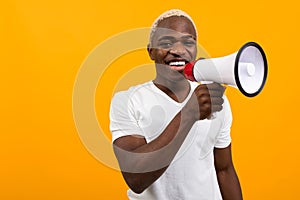 Black handsome smiling american man in white t-shirt speaks news through a megaphone on isolated orange background