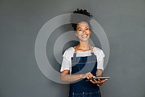 Black happy waitress in apron using digital tablet to take orders