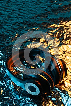 Black headphone in neon lights on the foil with shiny crumpled surface background. 80s music concept.