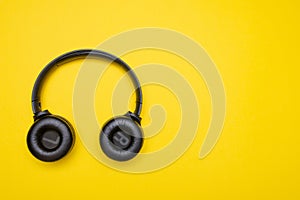 Black headphones on the left side of the photo. From above . Yellow background. Copy space