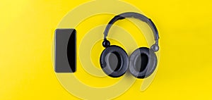 Black headphones and mobile phone on a yellow background. Concept of musical streaming