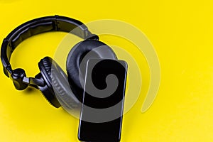 Black headphones and mobile phone on a yellow background. Concept of musical wireless streaming, listening to music through