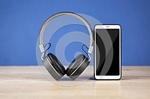 Black headphones and smart phone with stack books on wooden table againts blue wall