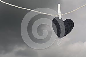 Black Heart paper hanging on a brown hemp rope on rain clouds ba