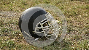 Black helmet lying on grass at pitch, symbol of American football game, sports