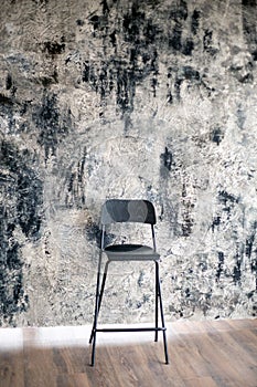 Black high-backed chair stands on a wooden floor against against a black-gray-white texture wall