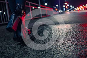 Black high heel boots illuminated with red traffic light on a dark walk path.Selected focus, Blurred town lights and traffic in