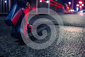 Black high heel boots illuminated with red traffic light on a dark walk path.Selected focus, Blurred town lights and traffic in