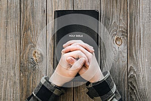 Black Holy Bible in male hands on a wooden background, top view.