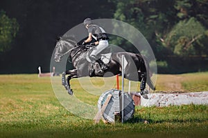 Black horse with man rider jumping over obstacle during eventing cross country competition