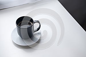 A black hot coffee cup with white saucer on vintage wooden table and curtain background in minimalism cafe