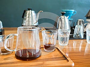The black hot coffee is extracted from the drip process in an espresso shot with a jar on wooden table.