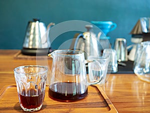 The black hot coffee is extracted from the drip process in an espresso shot with jar on wooden table