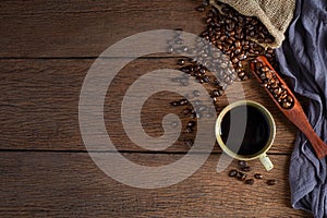 Black hot fresh coffee in brown ceramic cup with coffee beans roasted in burlap sack bag on wooden table background.