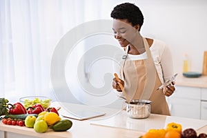 Black Housewife Cooking Browsing Recipes Online Via Tablet In Kitchen