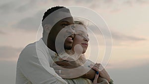 Black husband hugs blonde wife and looks at horizon closeup