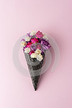 Black ice cream cone with colorful flowers on pastel pink background. Minimal summer composition