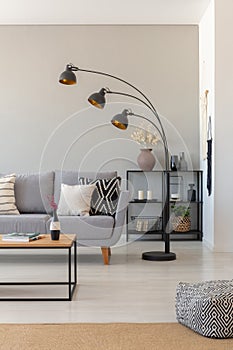 Black industrial lamp next to couch with patterned pillows in monochromatic living room, real photo