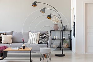 Black industrial lamp next to grey couch with patterned pillows, coffee table and pouf in monochromatic living room