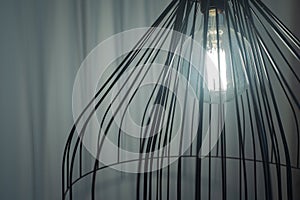 Black interior design fancy lamp with shining light bulb and white curtains in the background