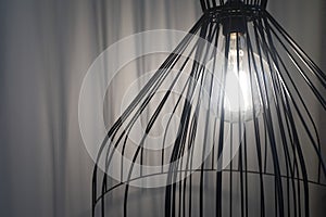 Black interior design fancy lamp with shining light bulb and white curtains in the background