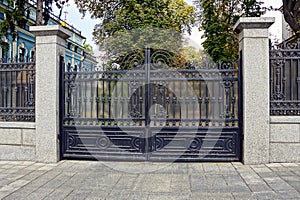 Black iron closed gates on a concrete fence near the sidewalk