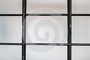 Black Iron grid with matte white glass panes fitted between bars, detail from a window.