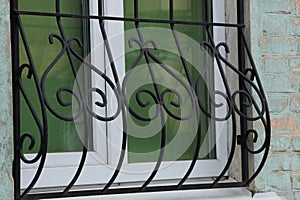 Black iron grill with forged pattern on a glass window
