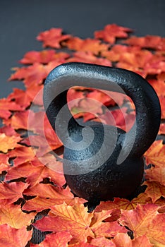 Black iron kettlebell on a black rubber gym floor, with orange and yellow maple leaves, fall fitness