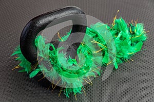 Black iron kettlebell with green feather boa on a black gym floor, holiday fitness