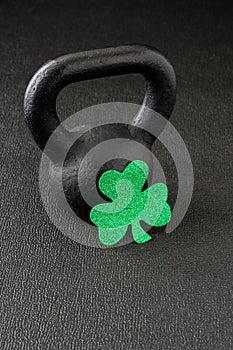 Black iron kettlebell and green glitter shamrock on a black gym floor, happy St. Patrick’s Day