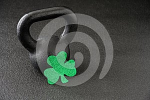 Black iron kettlebell and green glitter shamrock on a black gym floor, happy St. Patrick’s Day