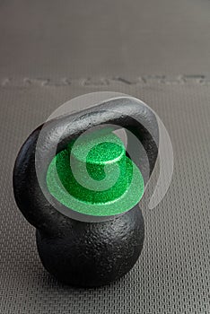 Black iron kettlebell with green leprechaun hat on a black gym floor, holiday fitness